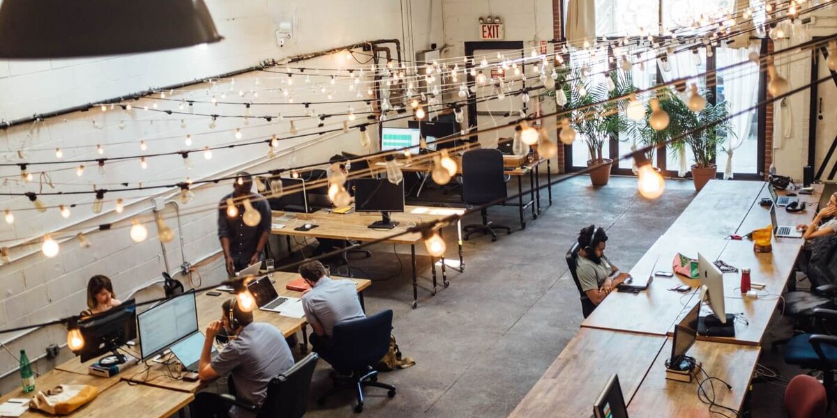 A big office space with wooden desks and a lot of lightbulbs. I'm glad I don't have to pay their energy bill.